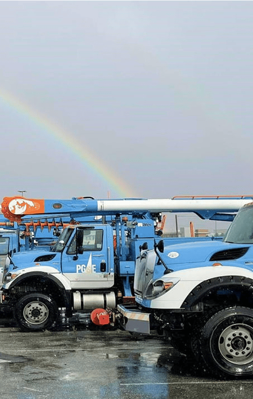 PG&E utility trucks parked on a wet lot under a rainbow