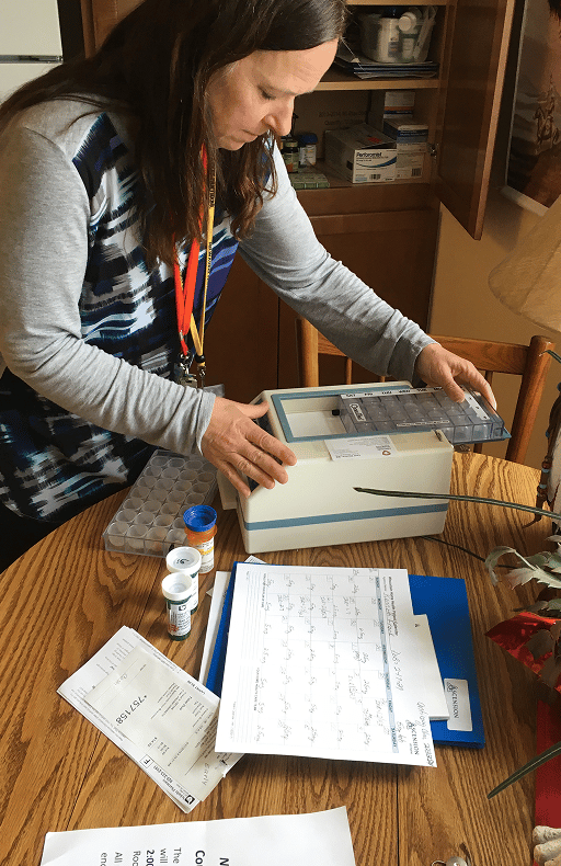 Health worker with a staff lanyard setting up a medication dispenser beside prescription bottles at a kitchen table