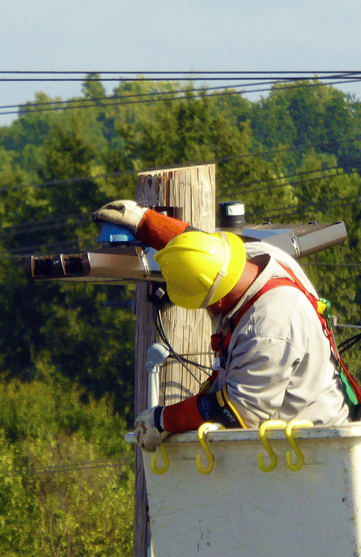 Utility lineworker in a hard hat and harness working on a power pole from a bucket truck