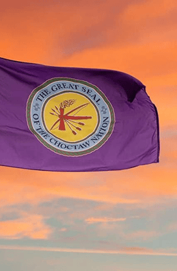 Choctaw Nation flag with the Great Seal of the Choctaw Nation against a sunset sky